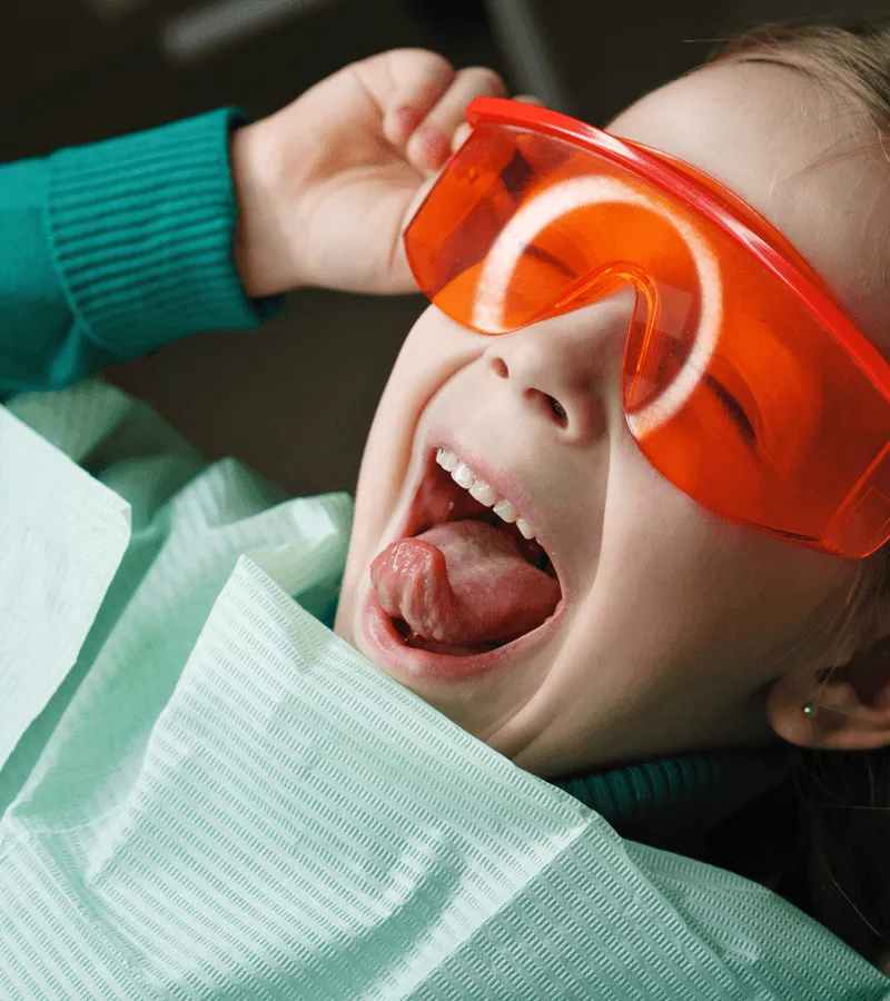 Little girl with orange glasses getting dental work done.